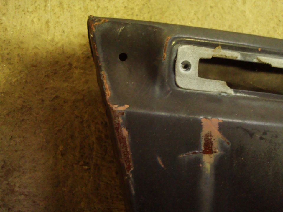 Dark gray car fender corner with rust spots and a mounting bracket hole