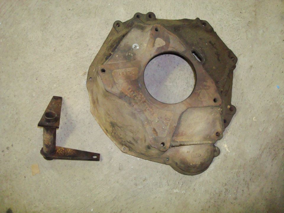 Cast iron transmission bell housing and a rusty metal linkage piece on a concrete floor