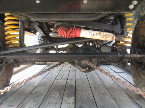 1978 Ford Bronco - The undercarriage of a vehicle is visible, yellow springs and a red-booted shock absorber, secured by chains to a wooden surface.