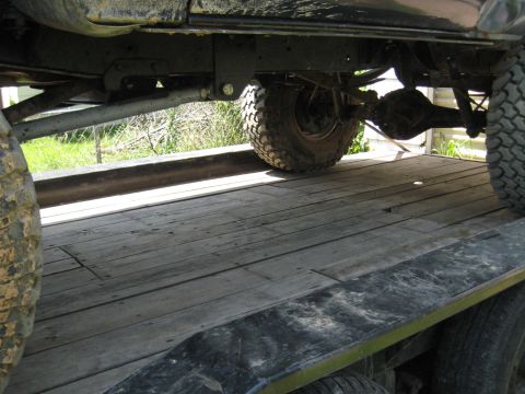1978 Ford Bronco - The underside of a vehicle is visible, showing its suspension and tires on a wooden trailer.