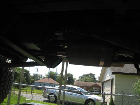 1978 Ford Bronco - The underside of a vehicle is visible, with two cars parked in the background behind a fence.