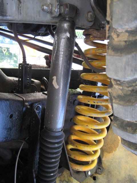1978 Ford Bronco - The suspension system of a vehicle, a shock absorber and a bright yellow coil spring, is shown in detail.