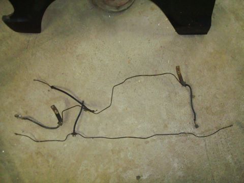 1995 Ford Bronco - Brake lines and a section of a vehicle fender are displayed on a concrete surface.