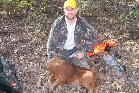 1982 Ford E350 - A hunter poses with his wild pig in a wooded area, with hunting gear scattered around.