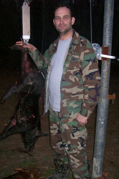 1982 Ford E350 - A man displays a hog he has hunted, suspended from a scale for weighing.