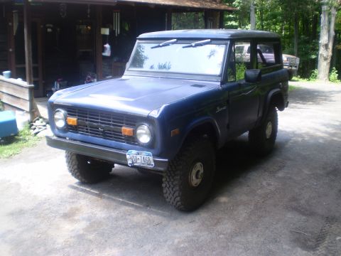 1979 Ford Bronco - A blue Ford Bronco is parked in front of a wooden structure with trees in the background.