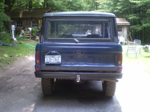 1979 Ford Bronco - Rear view of a blue 1979 Ford Bronco parked in a wooded area with two sheds in the background.