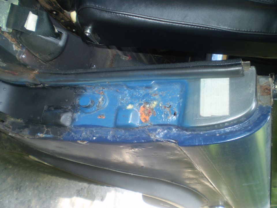 Close-up of rusted blue metal door sill with black trim and part of a black seat visible