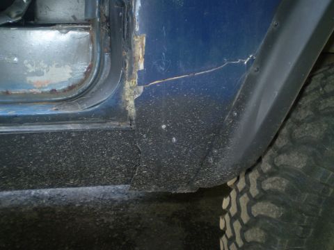 1979 Ford Bronco - Close-up of a blue vehicle's damaged door and fender, with a tire visible on the right.