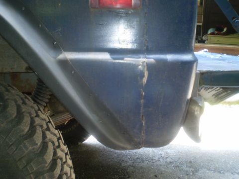 1979 Ford Bronco - Close-up of a blue vehicle's rear fender and tire, revealing damage and wear.