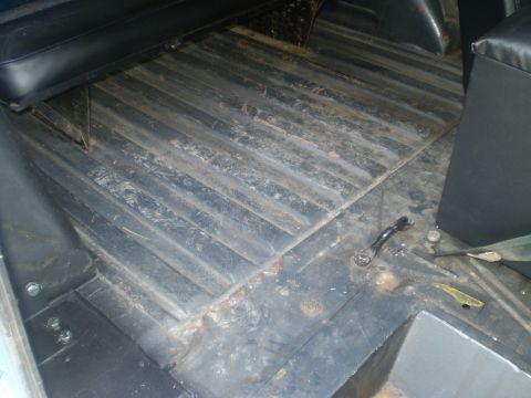 1979 Ford Bronco - The interior floor of a vehicle shows ribbed metal construction and black seating, with visible rust spots.