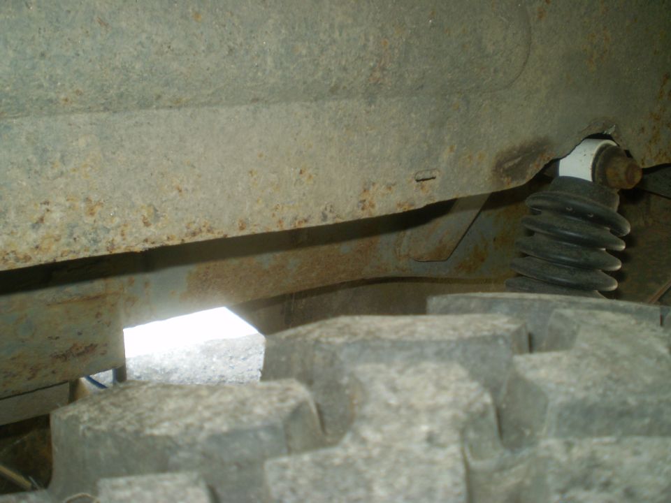 Close-up of rusted vehicle frame above a large tire. Shock absorber visible