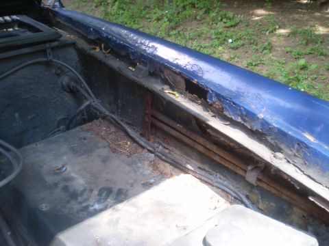 1979 Ford Bronco - The engine bay of a blue vehicle shows extensive rust damage along the fender and inner panels.