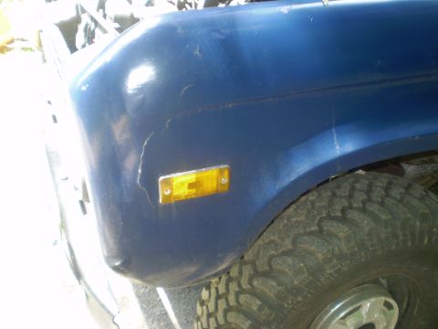 1979 Ford Bronco - Close-up of a blue SUV's front fender and tire, showing some wear and tear.