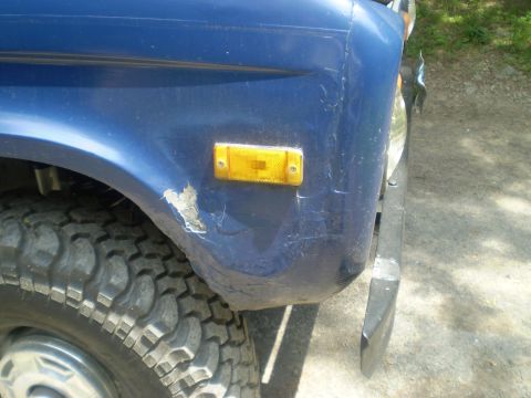 1979 Ford Bronco - Close-up of a blue SUV's front fender and tire, showing damage and an amber signal light.