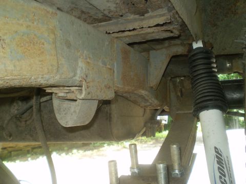 1979 Ford Bronco - Close-up of a rusty vehicle undercarriage, focusing on suspension components and frame damage.