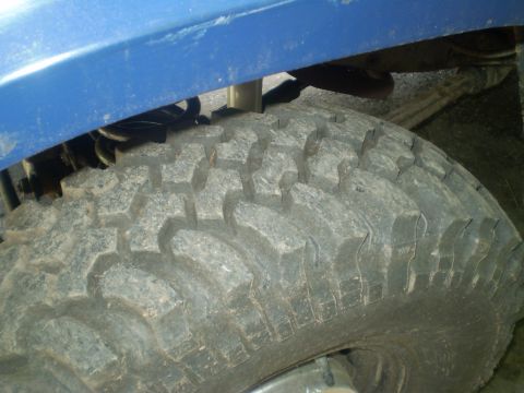 1979 Ford Bronco - Close-up of a vehicle's tire and suspension system, showing off-road tread and blue body panel.