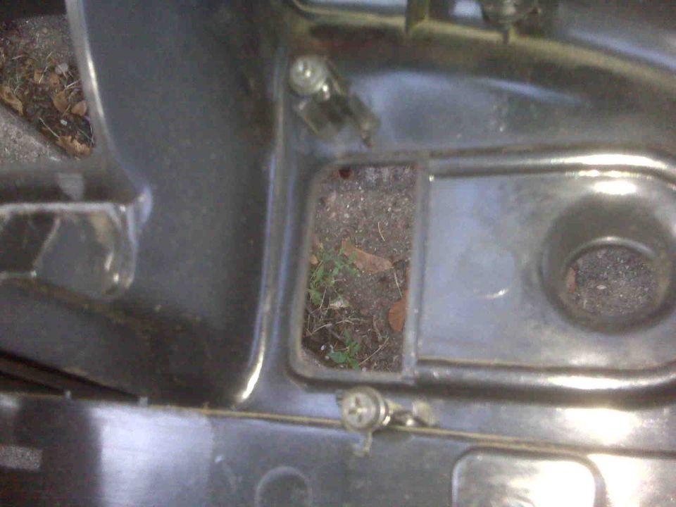 Close-up of a car's interior showing dirt and debris in a recessed area, with a visible screw