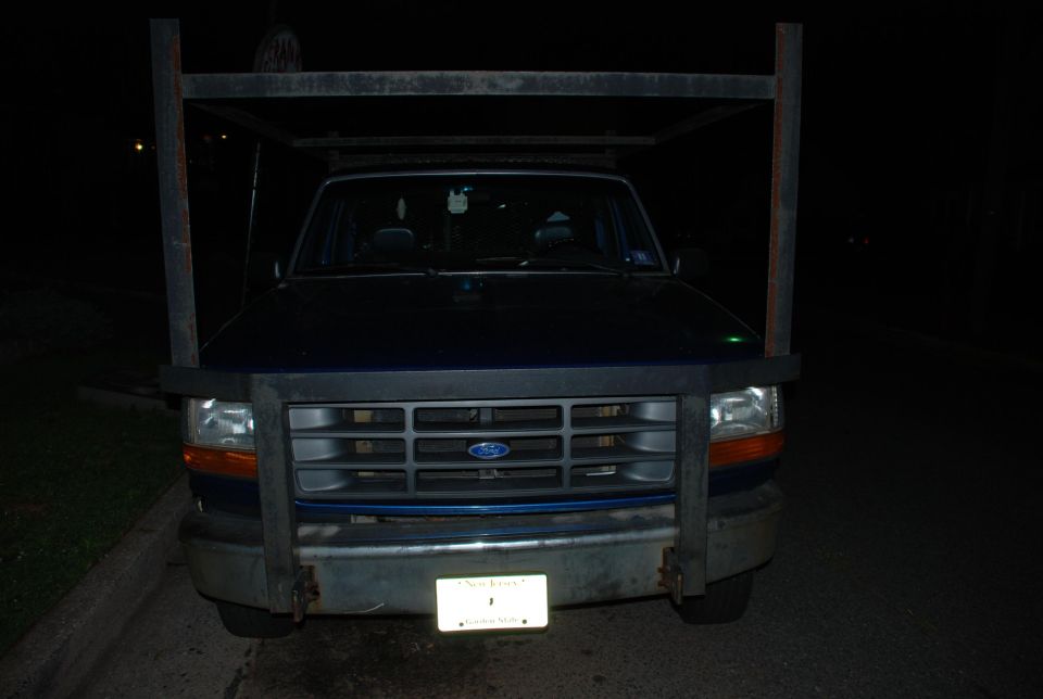 Dark blue 1990s Ford pickup with steel overhead rack, front view at night, New Jersey plate