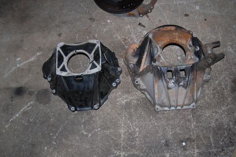 1994 Ford Bronco - Comparison of two transmission bell housings, one black and one weathered aluminum, resting on a concrete floor.
