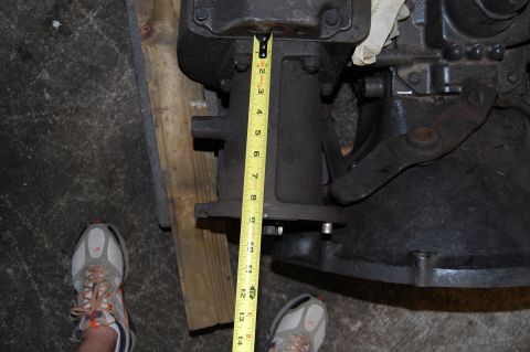 1994 Ford Bronco - A close-up shows a transmission component being measured with a yellow tape measure, with a person's shoe visible in the lower left corner.