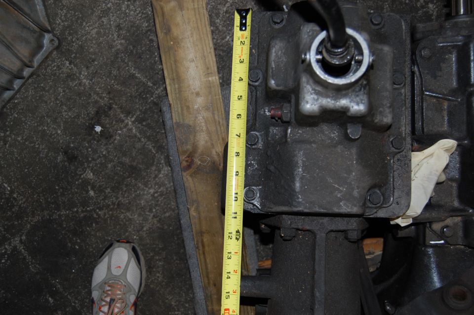 Close-up of a transmission housing with a yellow tape measure next to it. A shoe is visible in the lower left
