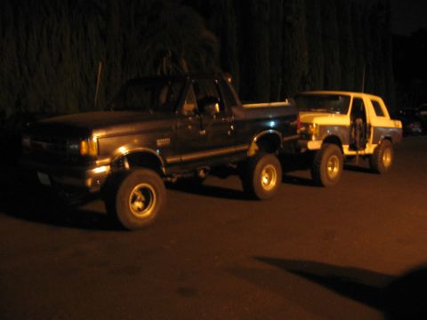 1989 Ford Bronco - Two Ford Bronco SUVs are parked next to each other in a dark outdoor setting.