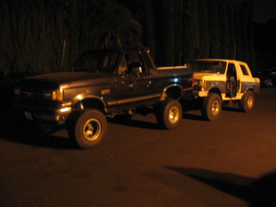 Dark blue and white Ford Bronco SUVs parked side-by-side at night