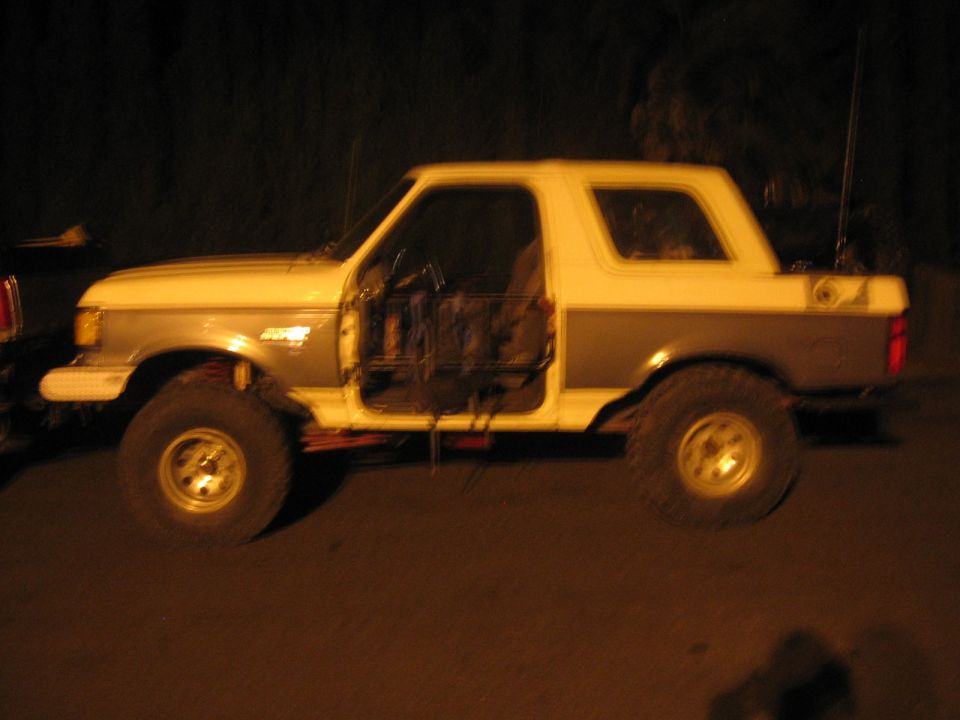 Side view of a lifted Ford Bronco with doors removed. It has a two-tone paint job and off-road tires