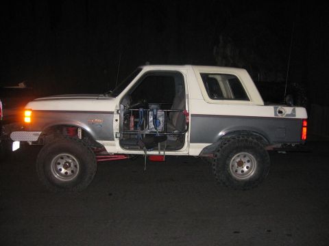 1989 Ford Bronco - A modified Ford Bronco is parked on a dark surface, its driver's door ajar.