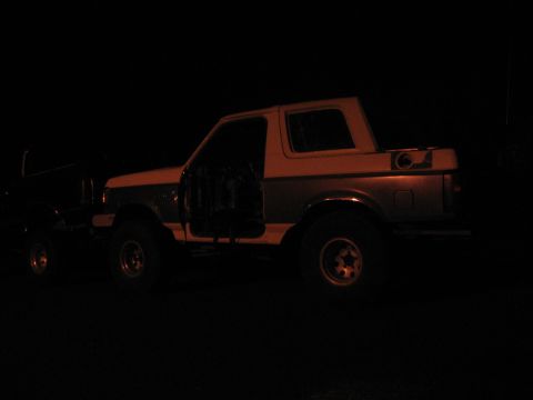 1989 Ford Bronco - Two vehicles parked at night, one is a 1989 Ford Bronco with its doors open.