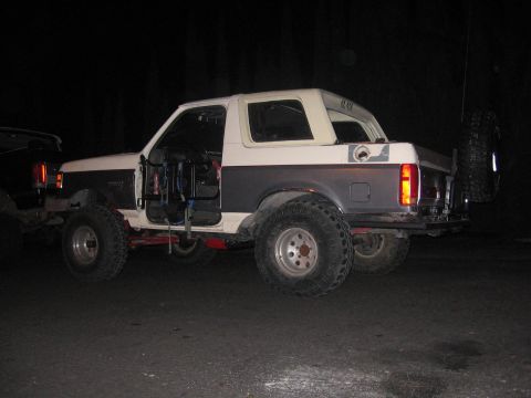 1989 Ford Bronco - This modified Ford Bronco is parked on a dark surface, possibly at night, with its doors open.