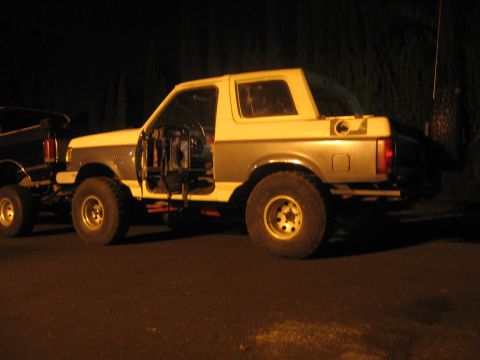1989 Ford Bronco - A modified Ford Bronco sits parked at night, its doors off and interior exposed.