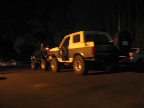 1989 Ford Bronco - A two-tone SUV, possibly a 1989 Ford Bronco, is parked at night with its driver's door open.