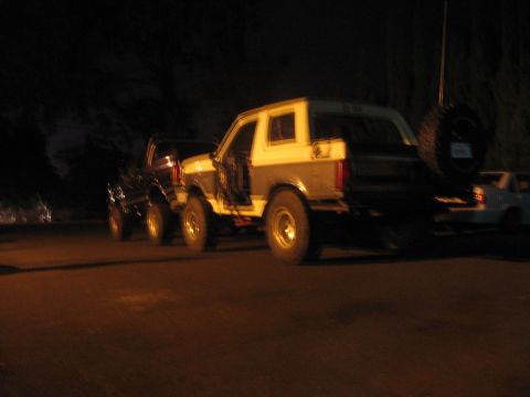 1989 Ford Bronco - Two SUVs, including a 1989 Ford Bronco, are parked side-by-side at night.