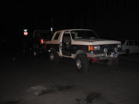 1989 Ford Bronco - A modified two-tone Ford Bronco is parked at night, with another vehicle visible behind it.