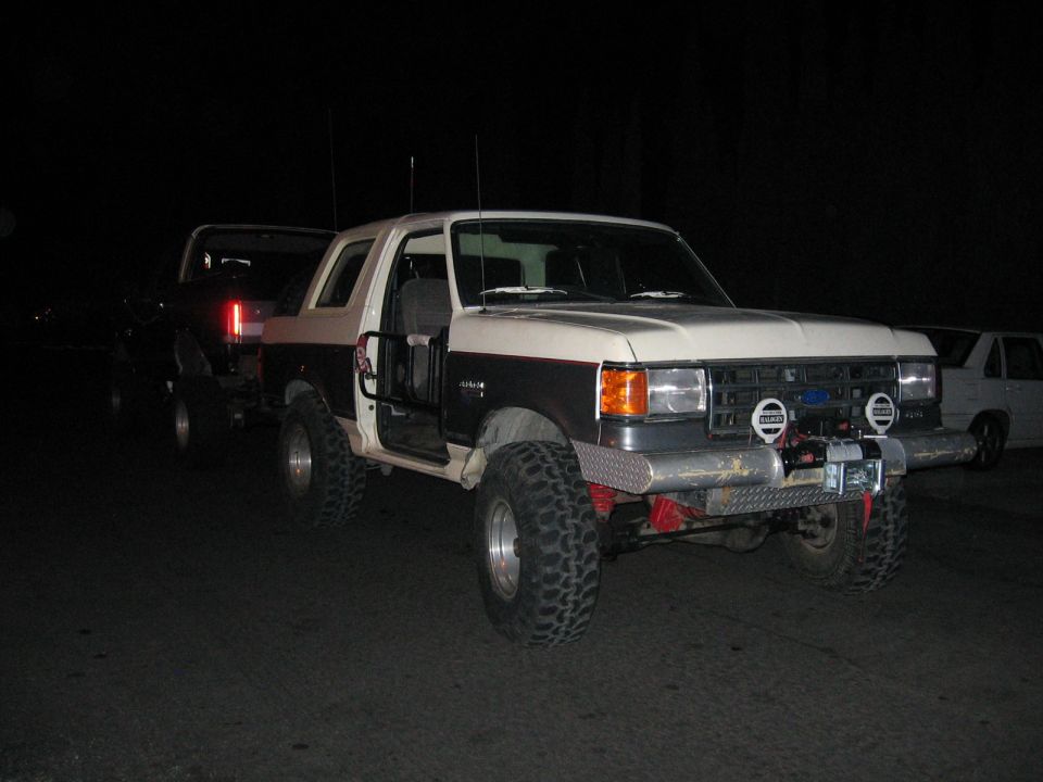 1989 Ford Bronco with off-road modifications, doors open, parked next to another SUV at night