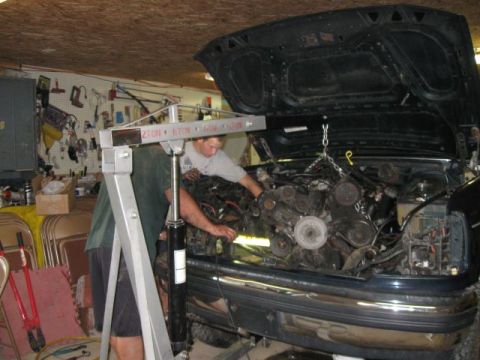 1992 Ford Bronco - Two people are working to remove the engine from a vehicle in a garage setting.