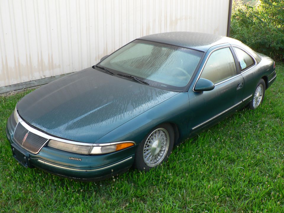 1990 Lincoln Mark VII coupe, green, parked on grass next to a white building