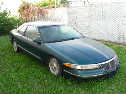 1990 Lincoln Mark VII - A green 1990 Lincoln Mark VII coupe sits on a grassy lawn next to a chain-link fence.