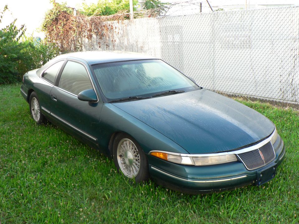 Green 1990 Lincoln Mark VII coupe parked on grass, front 3/4 view