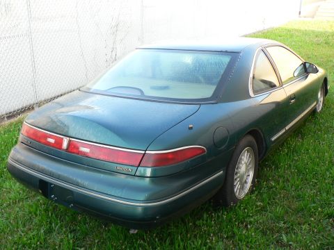 1990 Lincoln Mark VII - Rear view of a green Lincoln coupe parked on grass next to a fence. The vehicle has a distinctive taillight design.