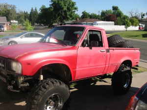1989 Ford Bronco - A red pickup truck is parked outside on a sunny day with a second vehicle visible in the background.
