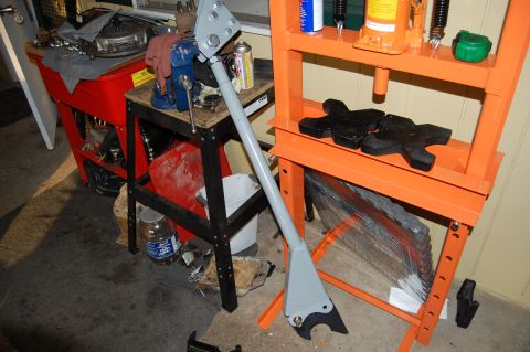 1994 Ford Bronco - A gray metal component is secured in a vise, with a hydraulic press and a red tool cart visible in the background.