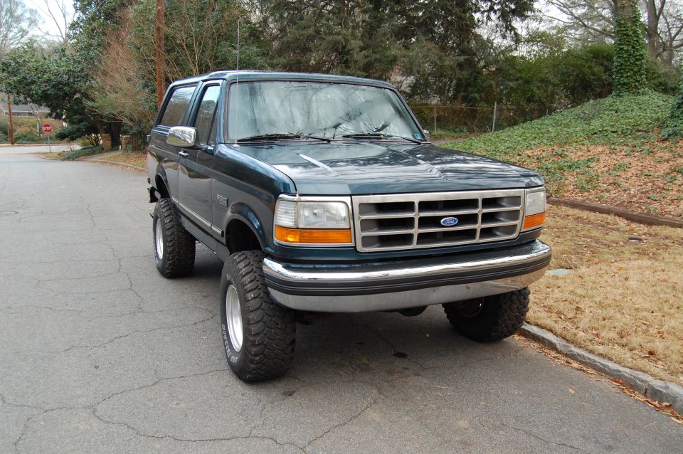 Dark green 1994 Ford Bronco with aftermarket wheels and tires parked on a residential street