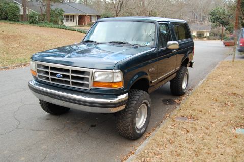 1994 Ford Bronco - This lifted Ford Bronco sits on a residential street, its dark green paint contrasting with the dry grass.