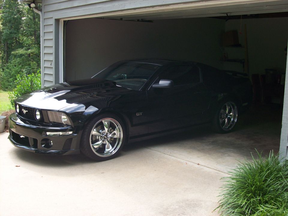 Black Mustang GT coupe with chrome wheels parked in a garage, 3/4 front view