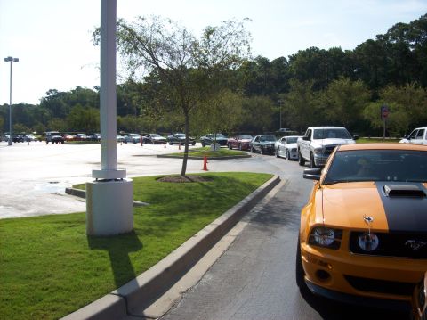 2007 Ford Mustang - A line of cars, including an orange and black Ford Mustang, are parked in a lot.