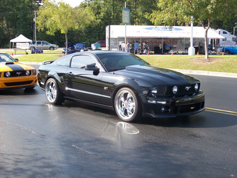 Black Ford Mustang GT with aftermarket hood and chrome wheels parked on asphalt