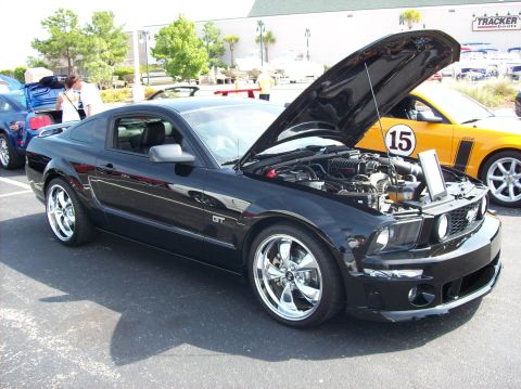 2007 Ford Mustang - A black 2007 Ford Mustang GT is parked with its hood open, revealing the engine. Another yellow car is visible in the background.